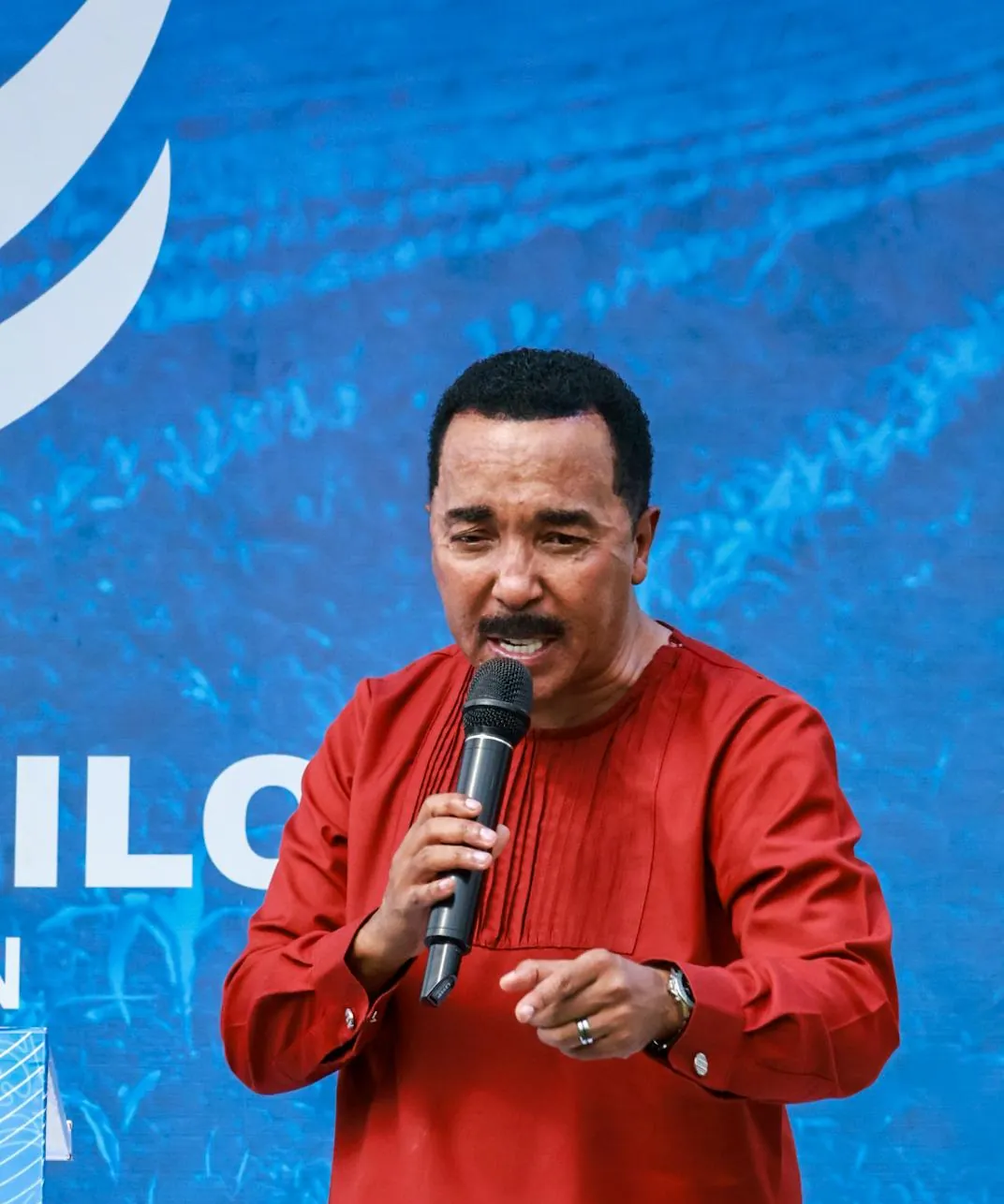 Dr David Molapo speaking on stage in a red outfit.